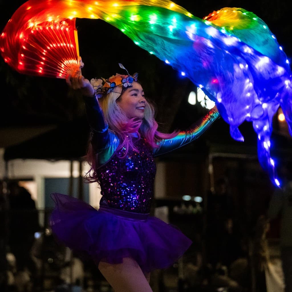 Performer with light-up rainbow fans at a night market